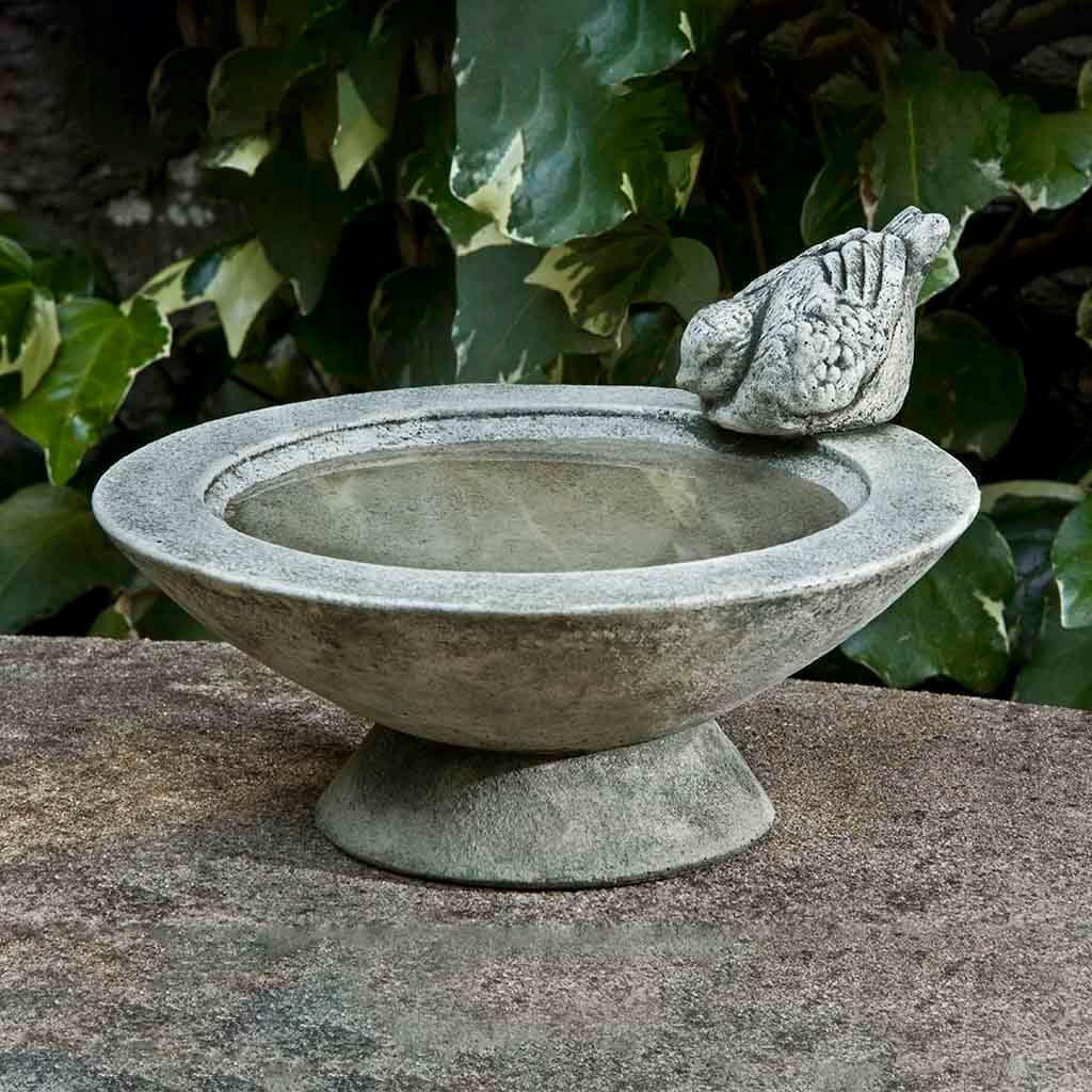 Stone bird bath with a stone bird on top in a garden setting
