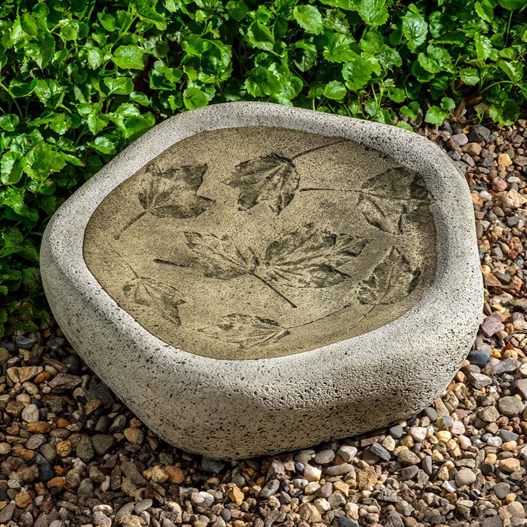 Concrete bowl with leaf design on a pebble and grass background