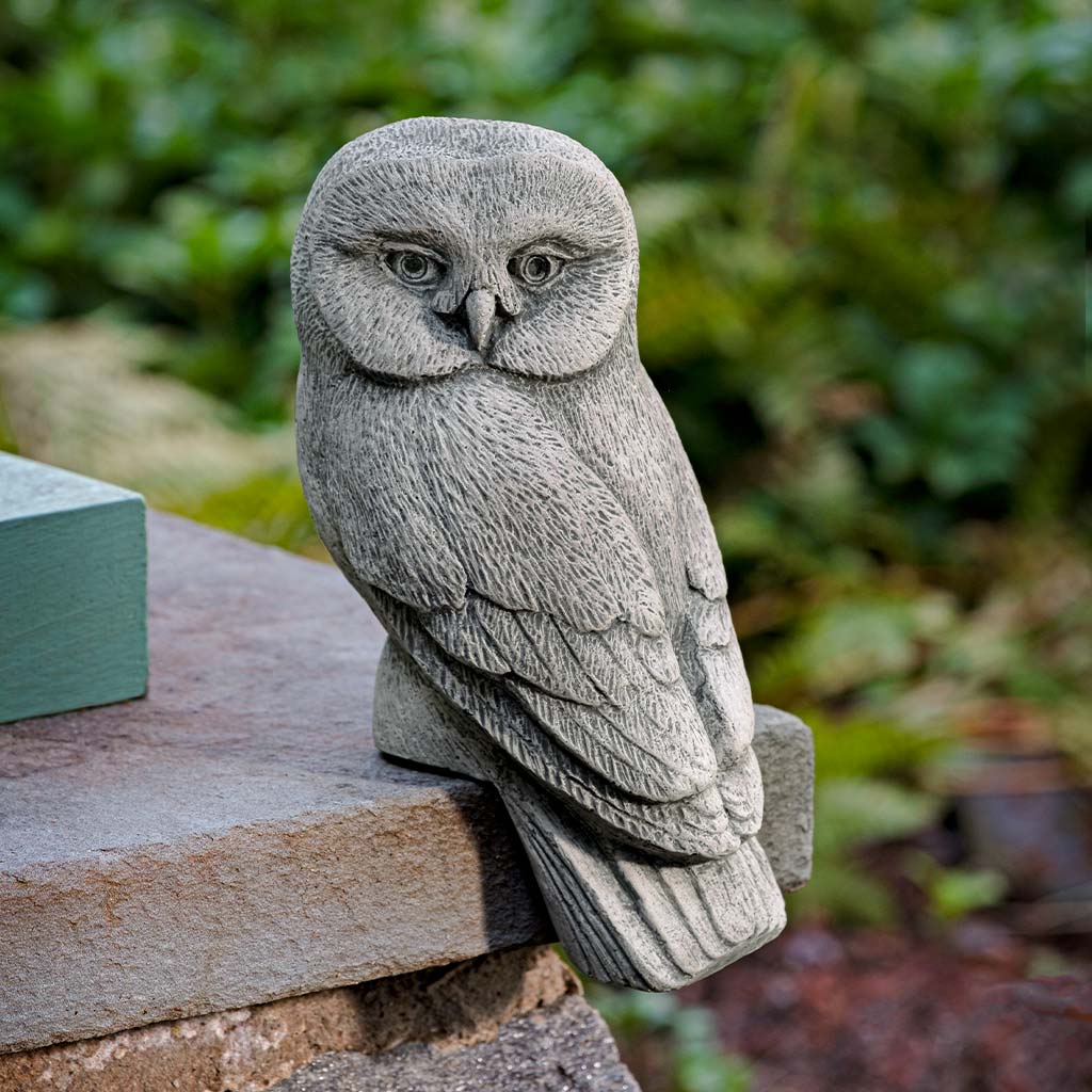 Stone owl sculpture on a natural stone surface with greenery in the background