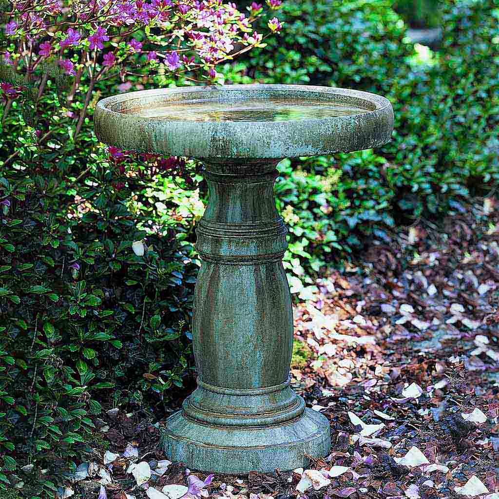 Decorative garden birdbath with a textured surface in a garden setting.