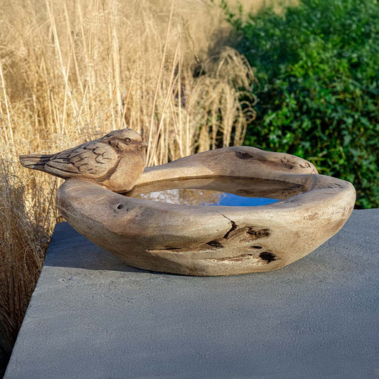 Wooden bird bath with a bird sculpture on a stone surface outdoors.