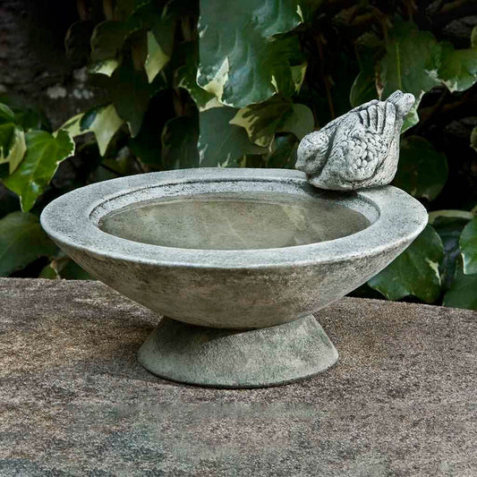 Stone bird bath with a stone bird on top in a garden setting