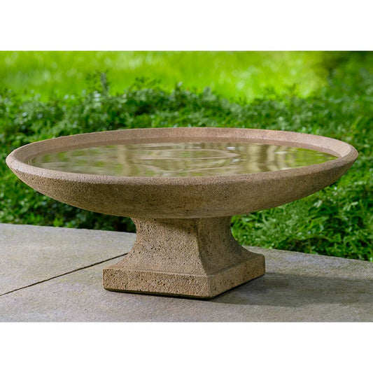 Stone bird bath on a concrete surface with grass in the background