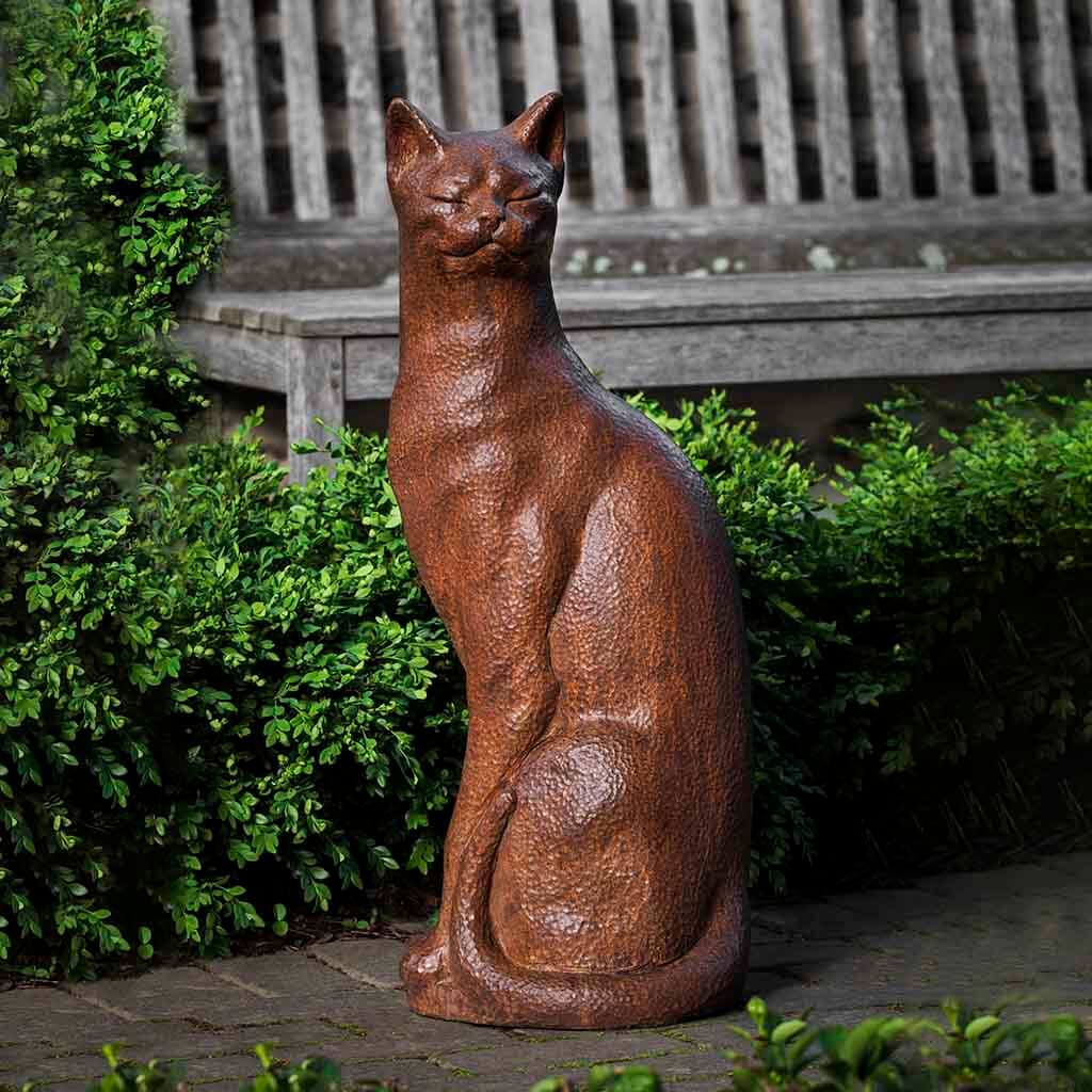 Bronze cat statue in a garden setting with a wooden bench in the background.